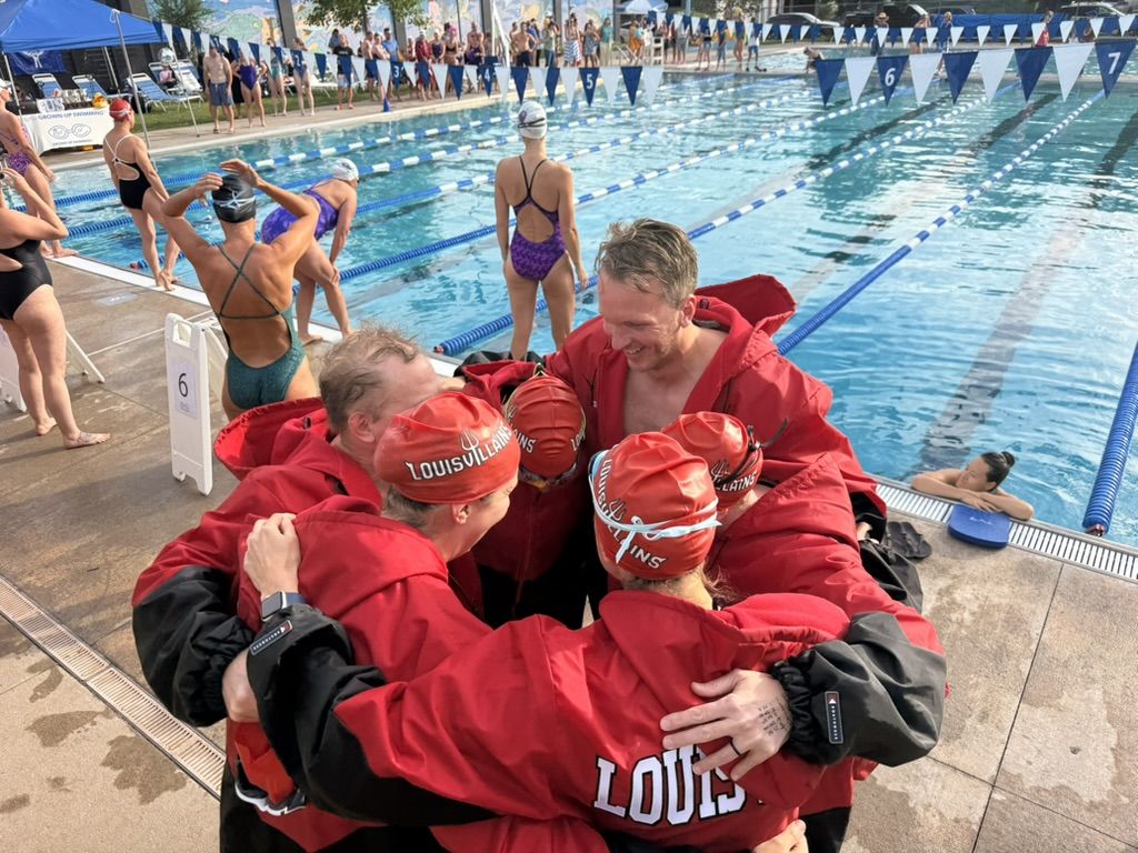 Louisvillains swimmers huddled together in red team parkas and caps beside the pool